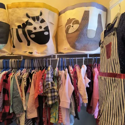 Assorted children's clothing hanging on a closet rack, with 3 Sprouts animal-themed storage bins featuring a zebra and a sloth...