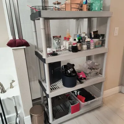 Four-tier grey plastic utility shelving unit holding various toiletries, bath products, and storage bins.