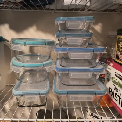 Assorted Pyrex glass food storage containers with locking blue lids, organized on a wire pantry shelf.