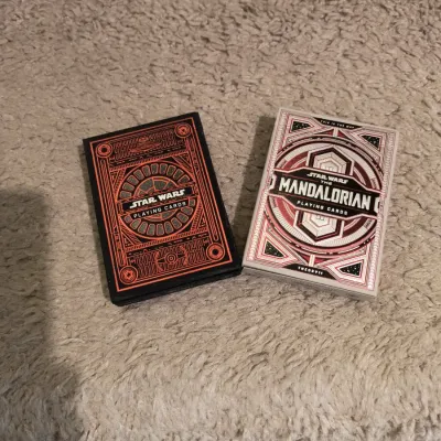 Two decks of Theory11 Star Wars themed playing cards, including a black and orange Star Wars deck and a white and red Mandalorian deck.