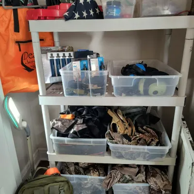 White plastic shelving unit holding outdoor and tactical gear, including LifeStraw water filters, hearing protection, camouflage...