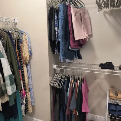Assorted women's clothing including dresses, sweaters, jeans, shorts, and t-shirts hanging in a closet, alongside a small shoe rack.