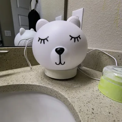 White silicone bear-shaped night light with closed eyes, sitting on a bathroom counter.