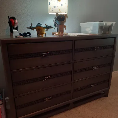 Modern dark brown six-drawer dresser featuring textured horizontal bands and silver-tone bow-tie pulls, styled with a space-themed lamp...