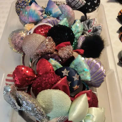 Collection of assorted Disney Minnie Mouse ear headbands in a clear plastic storage bin, featuring various sequined, themed, and holiday...