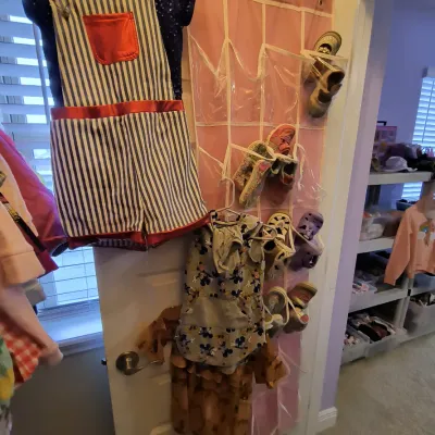 Assorted children's clothing and shoes, including a striped overall set and a pink over-the-door shoe organizer.