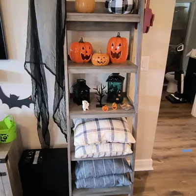 Rustic gray wooden ladder shelf styled with Halloween decorations, including jack-o'-lanterns and lanterns, alongside plaid and...