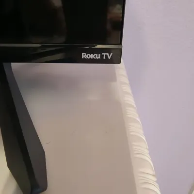 Close-up of a Roku TV smart television showing the brand logo on the bottom bezel and the stand leg.