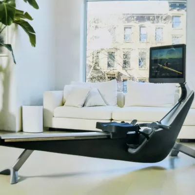 Hydrow smart rowing machine with a sleek black and silver frame, featuring its signature large touchscreen display, positioned in a...