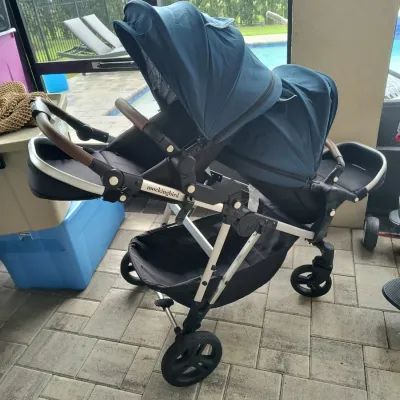 Mockingbird double stroller in navy blue and black with a silver frame, featuring dual adjustable canopies and a large under-seat storage...