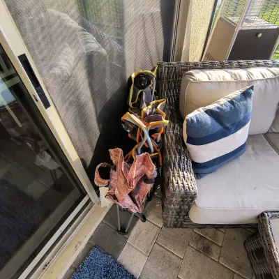 Three folded, portable camping chairs tucked behind a wicker patio sofa on a tiled outdoor patio.