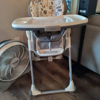 Graco high chair featuring an animal-themed padded seat cover, adjustable tray, and folding frame, shown alongside a white Cyclone floor...