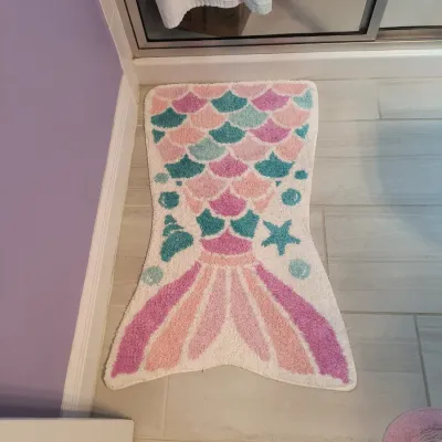 Mermaid tail-shaped bath mat featuring pastel pink, purple, and teal scales and fins on a white background.