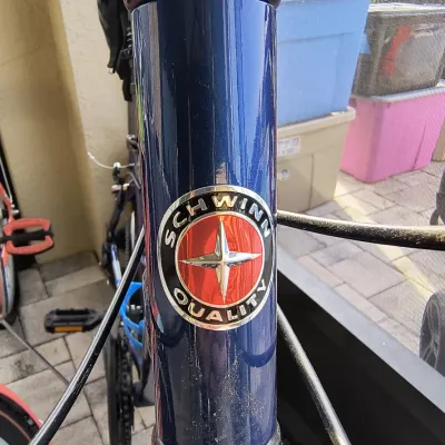 Close-up of a blue Schwinn bicycle frame showing the classic round "Schwinn Quality" head badge with a red and silver starburst...