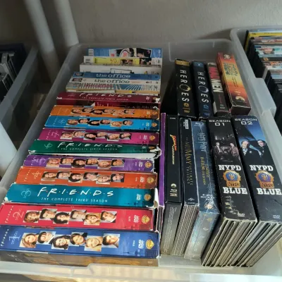 Collection of television series DVD box sets, including Friends, The Office, Heroes, and NYPD Blue, stored in a clear plastic bin.