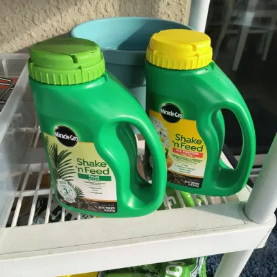 Two jugs of Miracle-Gro Shake 'n Feed plant food, including one Palm formula and one All Purpose formula, sitting on a white wire...