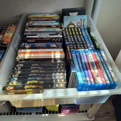 Assorted collection of DVDs and Blu-ray discs, including the Harry Potter series, Modern Family, and various family films, organized in a...