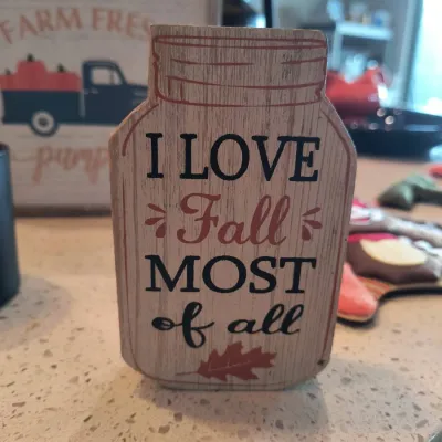 Rustic wooden block sign shaped like a mason jar, featuring the phrase "I Love Fall MOST of all" in black and orange lettering...