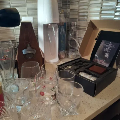 Assorted barware including a white SodaStream sparkling water maker, a cocktail smoker kit in its original box, and various drinking...