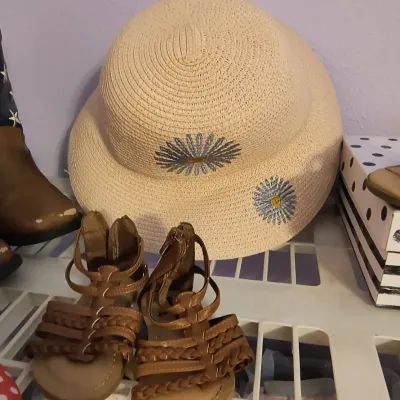 Children's woven straw sun hat with embroidered daisy details, paired with brown strappy gladiator-style sandals.