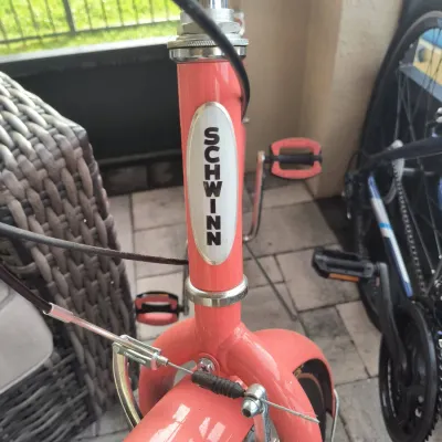 Vintage-style Schwinn cruiser bicycle featuring a coral pink frame with a classic white and black head tube badge.