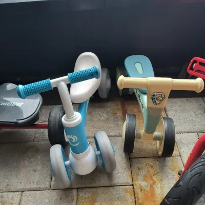Two toddler balance bikes, one in blue and white and the other in teal and cream, showing light wear from outdoor use.