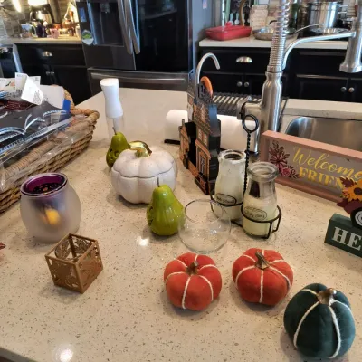 Assortment of autumn and Halloween-themed home decor, including fabric pumpkins, ceramic pears, a white pumpkin jar, and jarred candles...