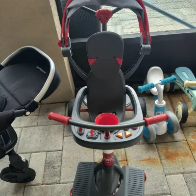 Radio Flyer convertible stroller trike with a red canopy, safety tray, and footrest, shown alongside other children's ride-on toys.
