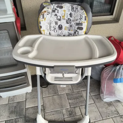 Graco high chair featuring a removable white tray with cup holder and an alphabet-patterned padded seat cushion.