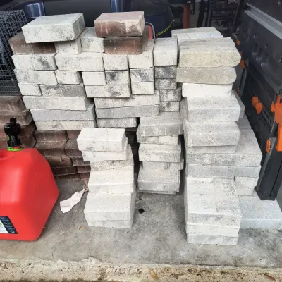 Large stack of concrete paving stones and bricks in various shades of gray and red, suitable for landscaping projects.