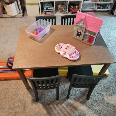 Child-sized wooden play table with four matching black wooden chairs, shown with various toys including a dollhouse and a plastic bin of...
