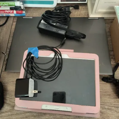 Lenovo laptop and a Samsung tablet in a pink protective case, both shown with their respective power adapters and charging cables.