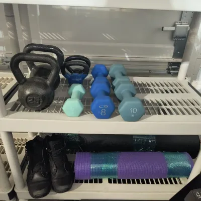 Assorted home gym equipment, including kettlebells, dumbbells ranging from 5 to 10 pounds, yoga mats, and a pair of black athletic boots,...