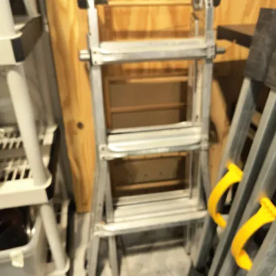 Multi-position aluminum folding ladder, showing some wear from use, stored in a garage or workshop setting.