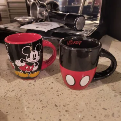 Pair of Disney Mickey Mouse ceramic mugs, one featuring a classic Mickey illustration and the other designed to look like his iconic red...
