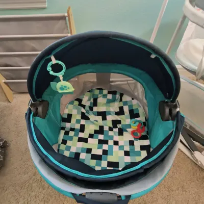 Fisher-Price On-the-Go Baby Dome in teal and navy blue, featuring a pixelated geometric pattern mat and hanging toys.