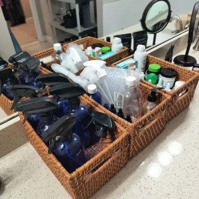 Set of woven wicker storage baskets containing various blue glass spray bottles and personal care products on a bathroom counter.