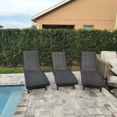 Trio of dark brown woven resin wicker chaise lounge chairs, positioned poolside on a paved patio.
