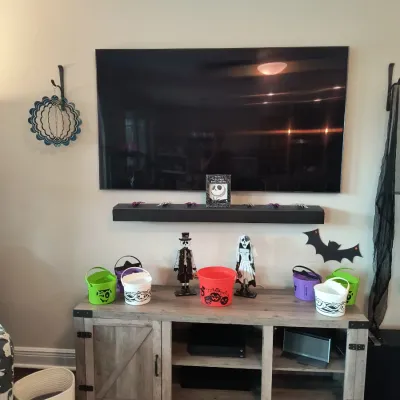 Modern farmhouse-style gray wood TV stand with sliding barn door, shown with a wall-mounted flat-screen TV, soundbar, and various...