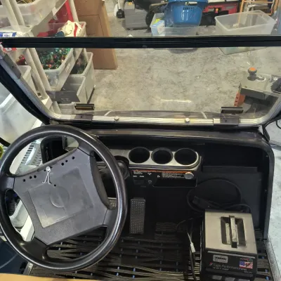 Interior view of a golf cart dashboard and steering wheel, featuring cup holders, floor pedals, and an Eagle Performance Series battery...