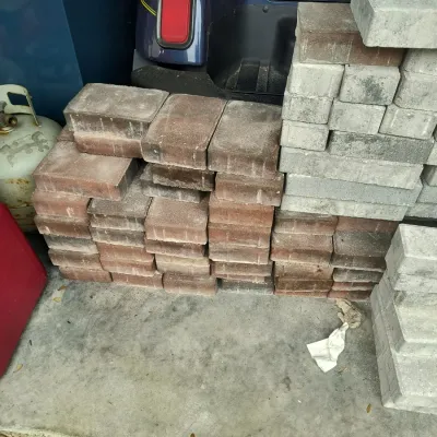 Stacks of unused concrete paving stones in red and grey tones, suitable for landscaping or patio projects.
