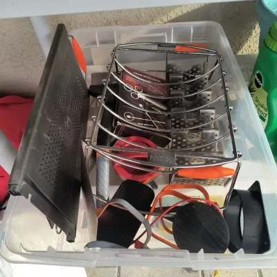 Assorted grilling accessories, including a Weber rib rack, grill grates, and cleaning tools, organized inside a clear plastic storage bin.
