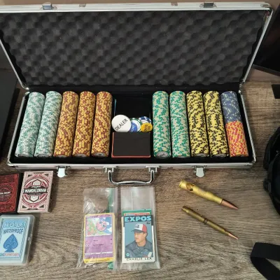 Poker chip set in an aluminum carrying case, shown alongside several decks of playing cards, vintage trading cards, and bullet-shaped pens.