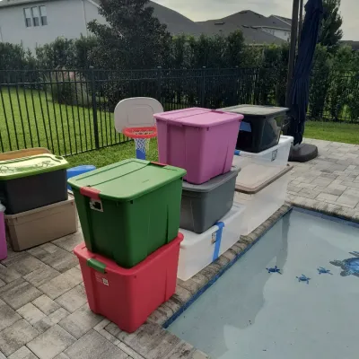 Assorted plastic storage bins in various colors and sizes, stacked on a paved pool deck.