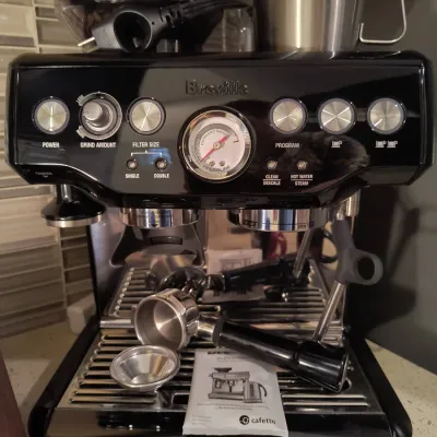Breville Barista Express espresso machine in black sesame finish, complete with portafilter, filter baskets, and cleaning accessories.