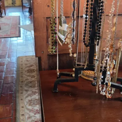 Assorted vintage and costume necklaces displayed on a black metal jewelry stand atop a wooden cabinet.