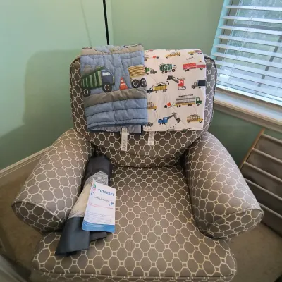 Upholstered armchair with a gray and white geometric pattern, shown with two children's quilts featuring construction vehicle motifs...
