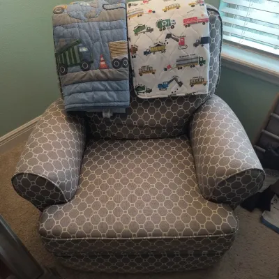 Upholstered armchair featuring a gray and white geometric pattern, draped with two children's quilts depicting construction vehicles...