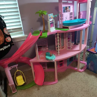 Barbie Dreamhouse playset featuring a multi-level pink structure with a slide, pool, swing, and palm tree accessory.