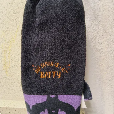 Halloween-themed black hand towel featuring embroidered orange text reading "Our Family Is A Bit Batty" and a purple border...